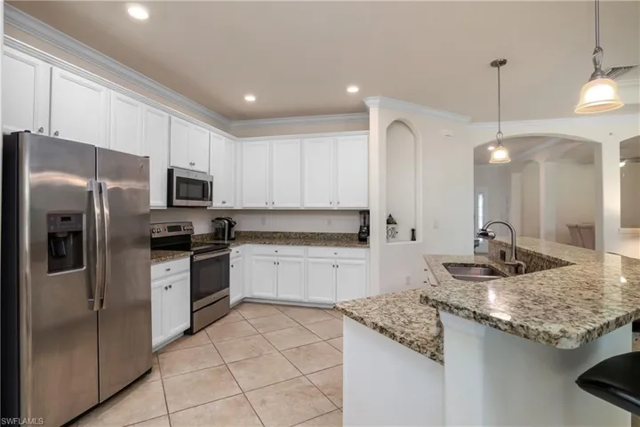 Kitchen featuring appliances with stainless steel finishes, white cabinetry, sink, and decorative light fixtures