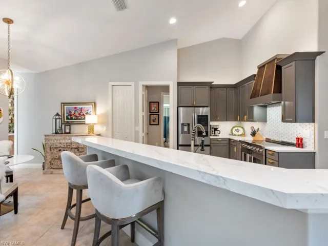 Kitchen featuring lofted ceiling, wall chimney range hood, backsplash, hanging light fixtures, and stainless steel refrigerator with ice dispenser