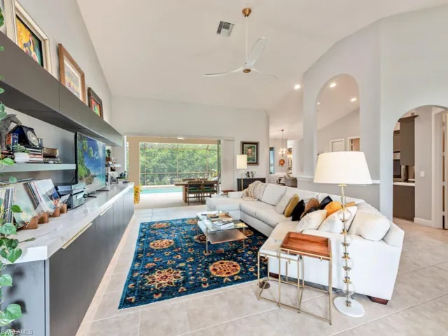 Tiled living room featuring ceiling fan with notable chandelier and vaulted ceiling