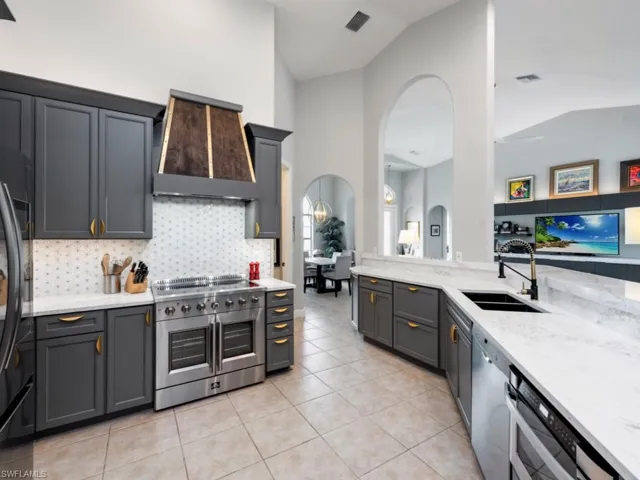 Kitchen with range with two ovens, wall chimney range hood, gray cabinets, backsplash, and light tile patterned floors
