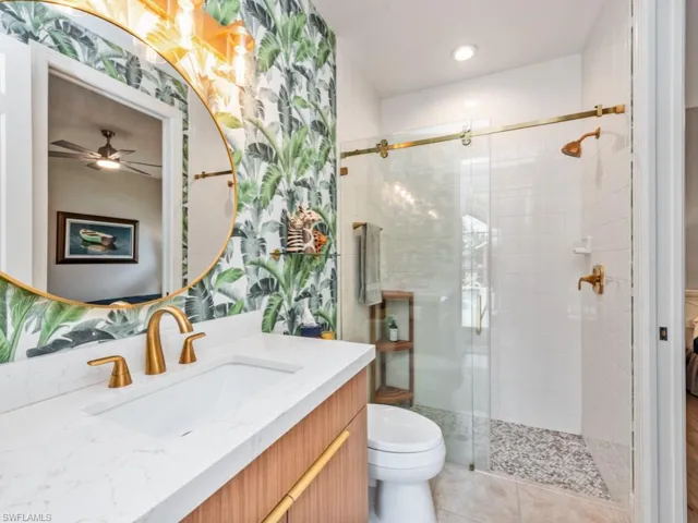 Bathroom with tile patterned flooring, a shower with door, toilet, vanity, and ceiling fan