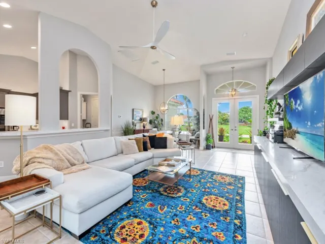 Tiled living room featuring high vaulted ceiling, french doors, and ceiling fan with notable chandelier