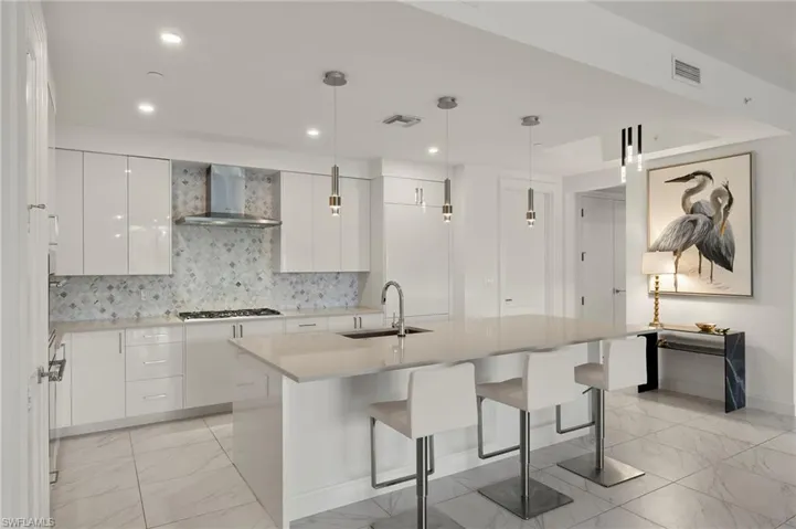 Kitchen featuring sink, white cabinetry, hanging light fixtures, a center island with sink, and wall chimney exhaust hood