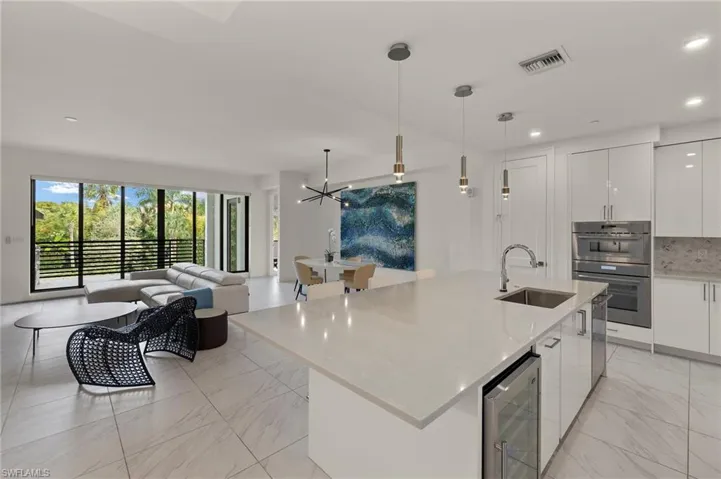 Kitchen featuring sink, white cabinetry, a center island with sink, pendant lighting, and beverage cooler
