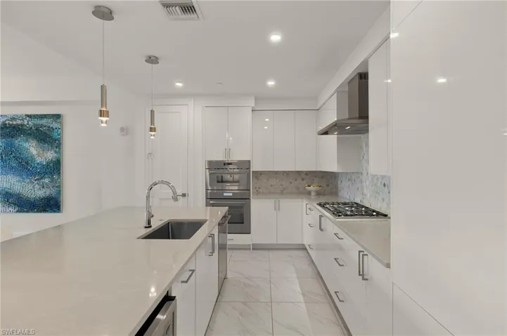 Kitchen with sink, white cabinetry, decorative light fixtures, stainless steel appliances, and wall chimney range hood