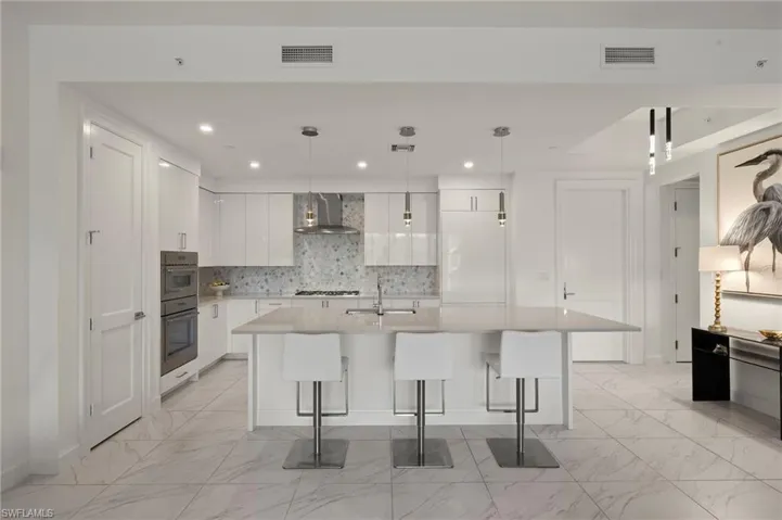 Kitchen with white cabinetry, hanging light fixtures, a center island with sink, a kitchen bar, and wall chimney exhaust hood