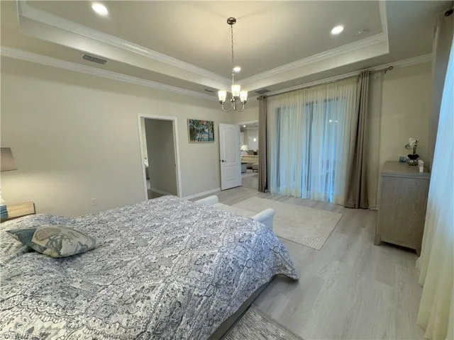 Bedroom with a tray ceiling, a chandelier, light wood-style floors, and ornamental molding
