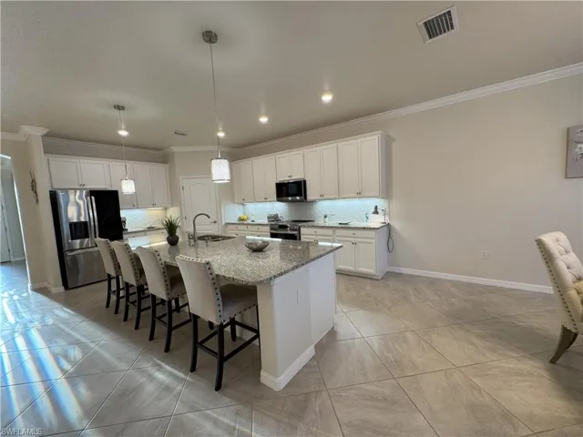 Kitchen featuring a breakfast bar, stainless steel appliances, decorative backsplash, white cabinets, and ornamental molding
