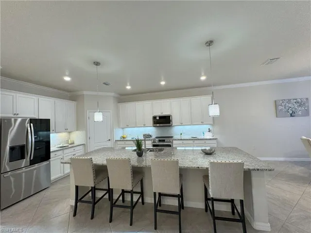 Kitchen with stainless steel appliances, a kitchen bar, a large island with sink, white cabinetry, and hanging light fixtures