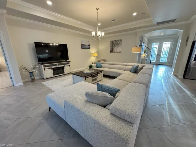 Living area featuring arched walkways, a tray ceiling, french doors, crown molding, and suspended lighting