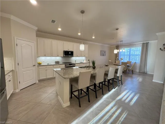 Kitchen with a breakfast bar area, a center island with sink, backsplash, ornamental molding, and light stone countertops