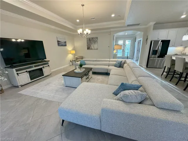 Living room featuring arched walkways, a tray ceiling, crown molding, and suspended lighting