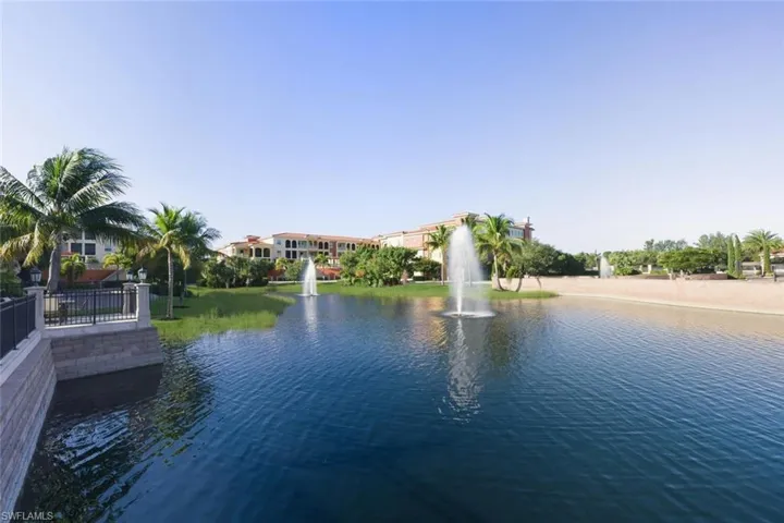 Waterfront property featuring multiple fountains, mature palm trees, manicured landscaping, and a sandy bank