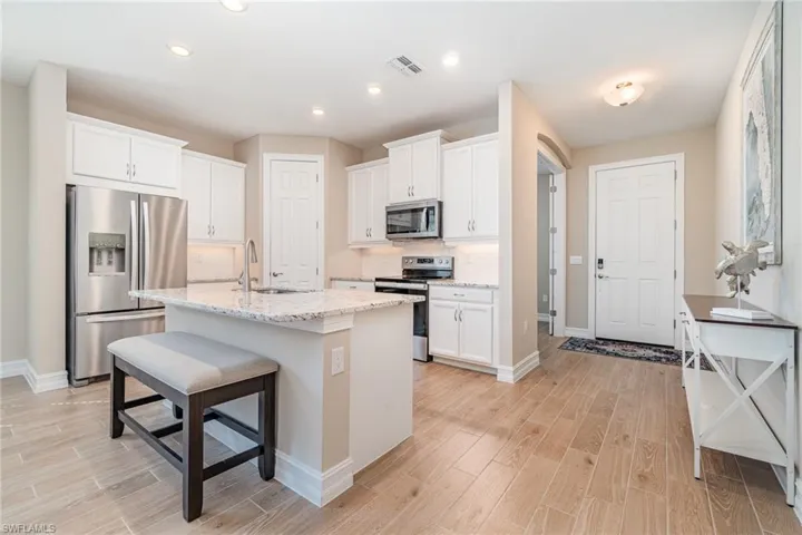 Kitchen featuring white cabinets, light stone countertops, stainless steel appliances, and sink