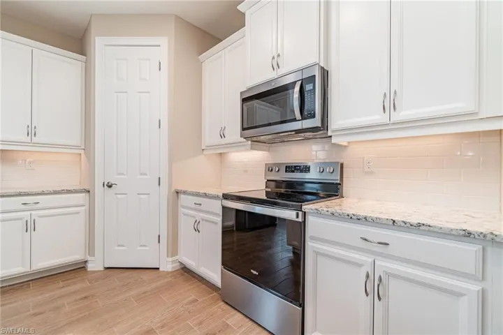 Kitchen featuring light hardwood / wood-style floors, appliances with stainless steel finishes, decorative backsplash, and white cabinets