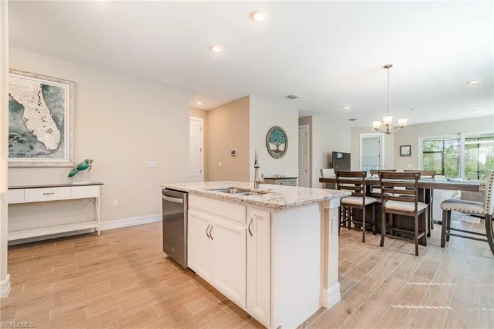Kitchen with a center island with sink, dishwasher, light hardwood / wood-style flooring, and hanging light fixtures