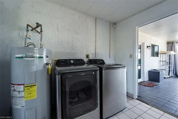 Laundry room with water heater, washing machine and dryer, light tile patterned floors, and a textured wall
