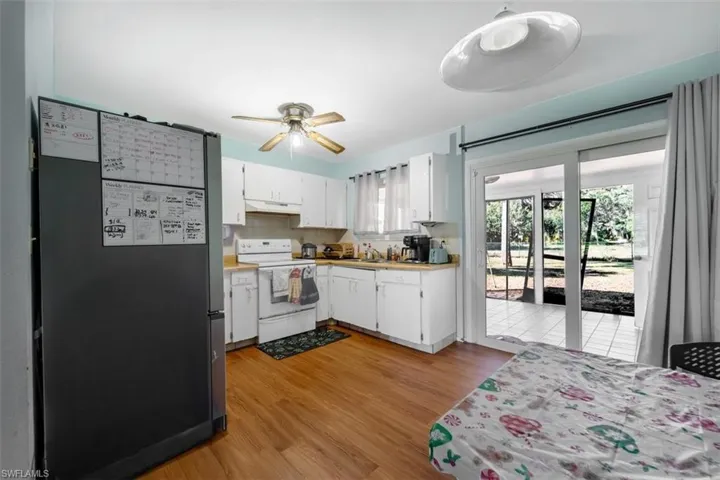 Kitchen featuring freestanding refrigerator, white cabinets, white electric range oven, and light countertops