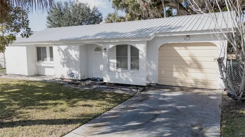 Ranch-style home featuring a metal roof, a front yard, stucco siding, concrete driveway, and an attached garage