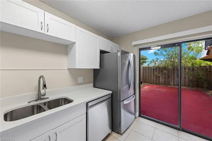 Kitchen with sink, appliances with stainless steel finishes, light tile patterned floors, and white cabinetry
