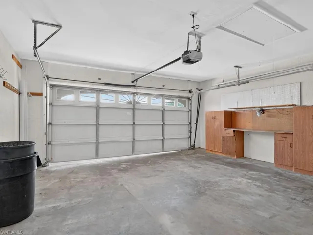 Concrete flooring, overhead garage door opener, wood-finish built-in cabinetry, and integrated workbench