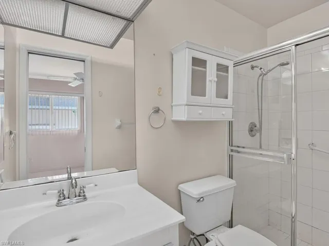 Vanity with integrated sink, chrome faucet, wall-mounted storage cabinet, and enclosed shower with tiled walls
