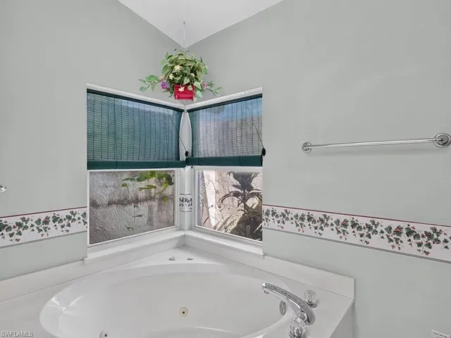 Corner jetted bathtub with a surround countertop, chrome fixtures, and corner windows