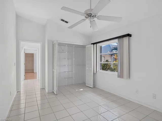 Vaulted ceiling, ceiling fan, white tile flooring, louvered bi-fold closet doors, and window with vertical blinds