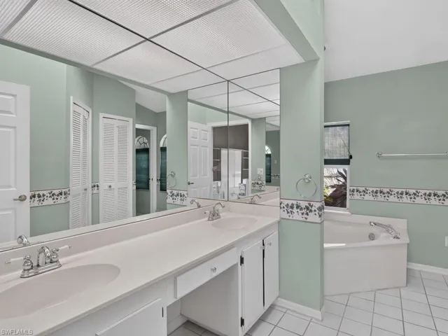 Dual vanity with integrated sinks, recessed lighting, white panel cabinetry, built-in bathtub, and tile flooring