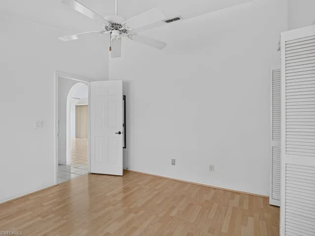 Sloped ceiling room featuring wood-finish flooring, a white ceiling fan, and louvered closet doors