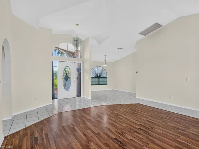 Vaulted ceiling with an arched entry, wood-finish flooring, and tile flooring