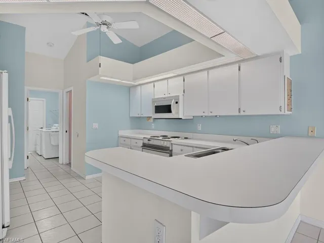 Kitchen featuring white cabinetry, integrated microwave, built-in cooktop, and a white countertop with an integrated sink