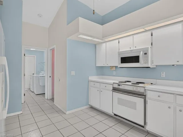 White cabinetry, stainless steel oven, white over-range microwave, white countertops, and tile flooring