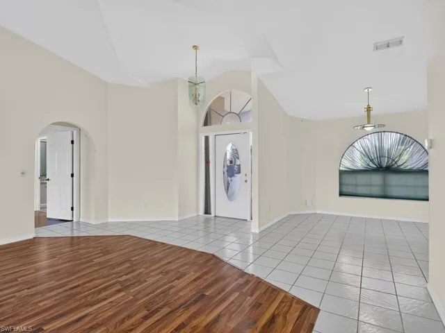 Vaulted ceiling with an arched entry, a decorative front door, and a semi-circular window