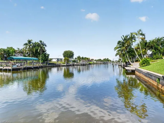 Waterfront property featuring a private boat dock with a covered slip, mature palm trees, and a landscaped grassy area