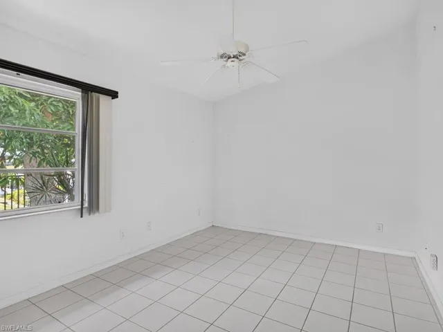 Vaulted ceiling, ceiling fan, window with exterior foliage, white tile flooring, white walls