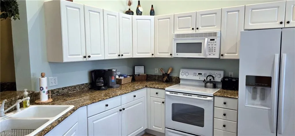 Kitchen with white appliances, white cabinets, and dark stone countertops