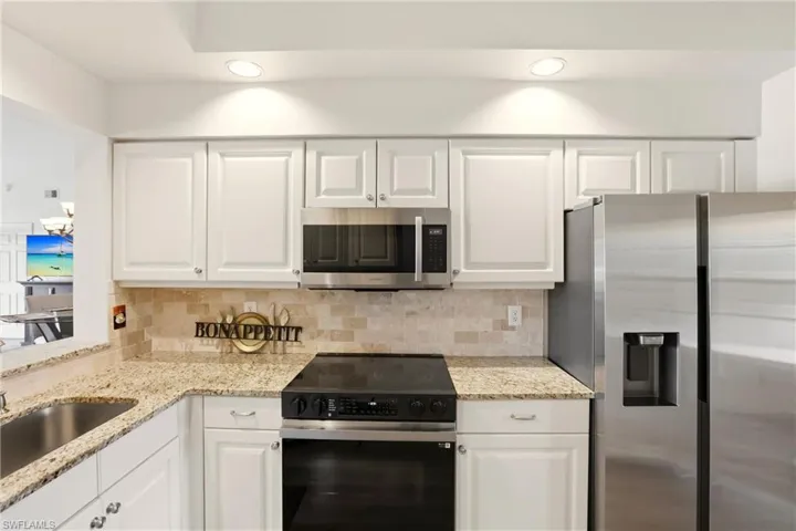 Kitchen with appliances with stainless steel finishes, white cabinets, light stone countertops, recessed lighting, and backsplash