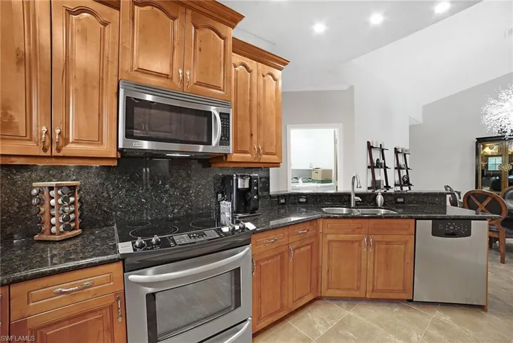 Kitchen with appliances with stainless steel finishes, dark stone counters, tasteful backsplash, sink, and light tile patterned floors