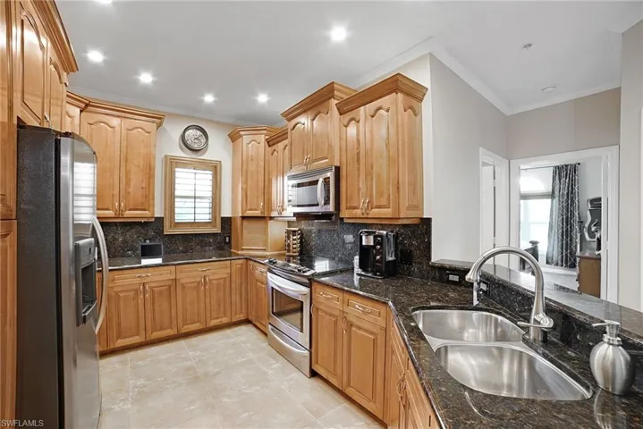 Kitchen featuring dark stone counters, stainless steel appliances, decorative backsplash, and a wealth of natural light