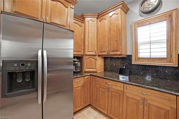 Kitchen featuring dark stone countertops, backsplash, light tile patterned floors, and stainless steel refrigerator with ice dispenser