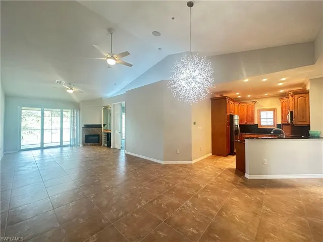 Unfurnished living room with sink, high vaulted ceiling, ceiling fan with notable chandelier, and light tile patterned floors
