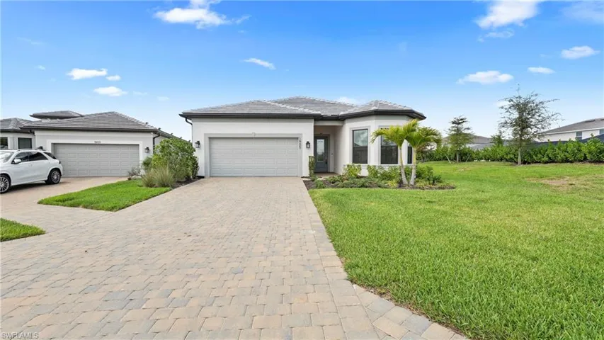 Prairie-style home featuring an attached garage, stucco siding, decorative driveway, and a front yard