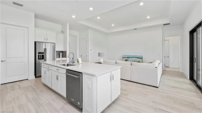 Kitchen with white cabinetry, a tray ceiling, open floor plan, stainless steel appliances, and a center island with sink
