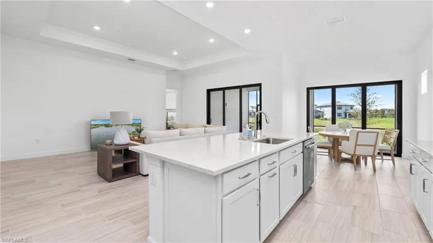 Kitchen with light stone countertops, open floor plan, a center island with sink, white cabinets, and recessed lighting