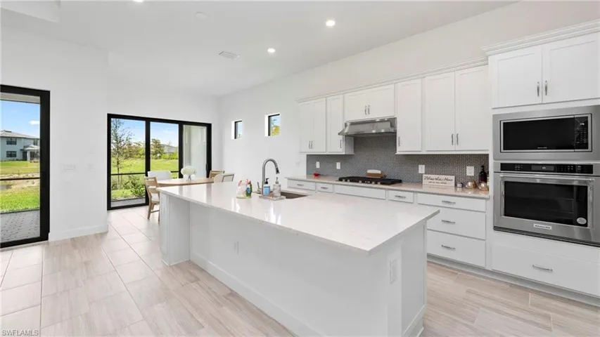 Kitchen with stainless steel appliances, white cabinetry, light stone counters, a center island with sink, and decorative backsplash