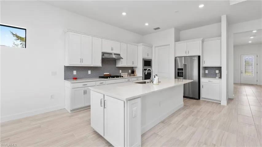 Kitchen featuring white cabinets, stainless steel appliances, a center island with sink, light stone countertops, and recessed lighting