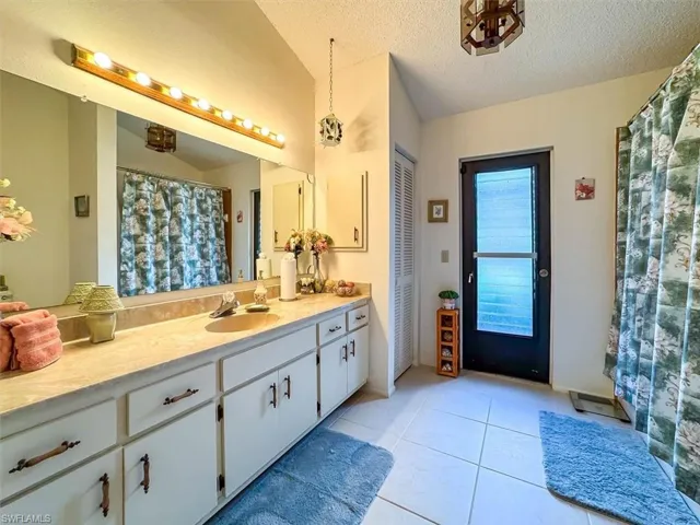 Bathroom featuring tile patterned flooring, vanity, a textured ceiling, and vaulted ceiling