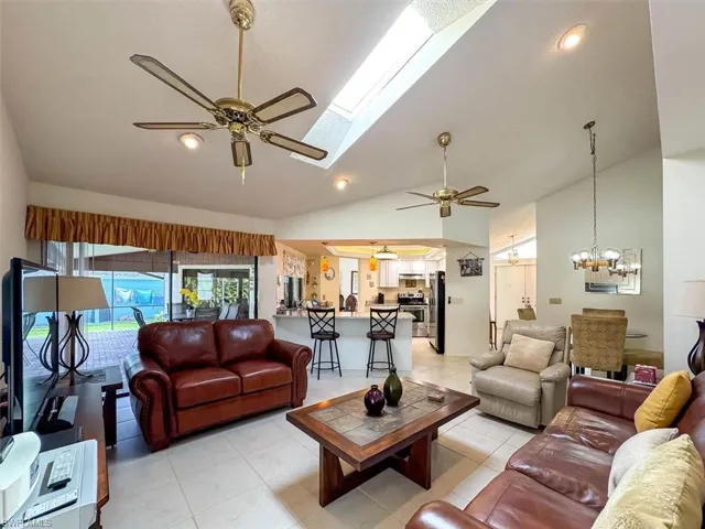 Living room with vaulted ceiling with skylight, light tile patterned floors, and ceiling fan with notable chandelier