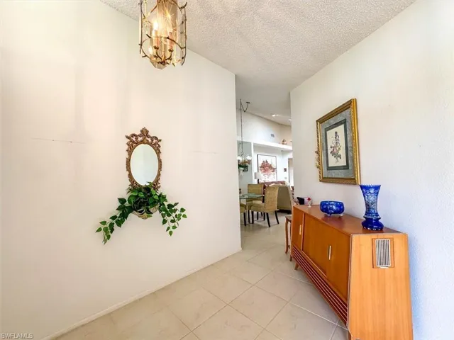 Hallway featuring light tile patterned floors, a textured ceiling, and a notable chandelier